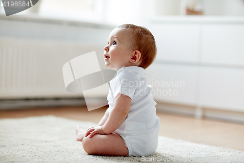 Image of happy baby boy or girl sitting on floor at home