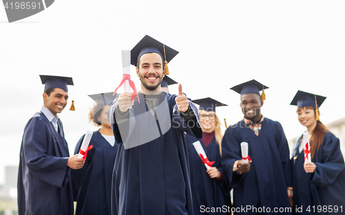 Image of happy students with diplomas showing thumbs up