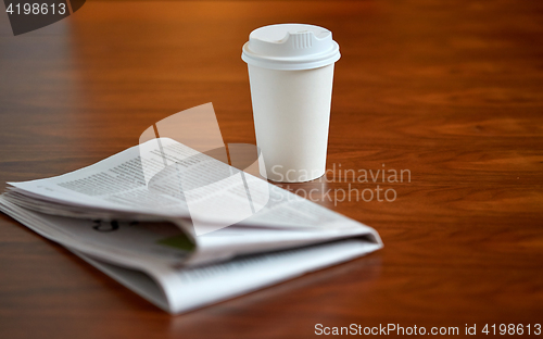 Image of coffee drink in paper cup and newspaper on table