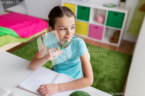 Image of happy girl with book writing to notebook at home
