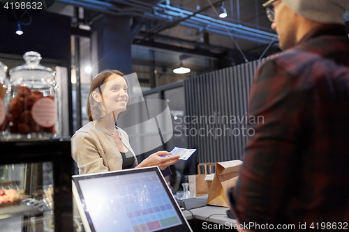 Image of happy woman paying money to seller at cafe