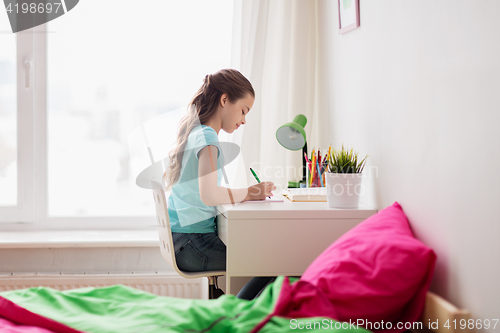 Image of happy girl with book writing to notebook at home