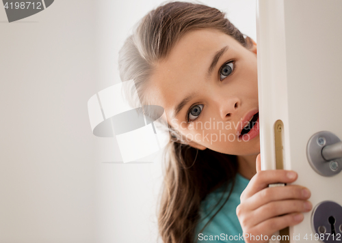 Image of scared beautiful girl hiding behind door at home
