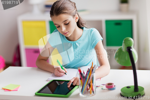 Image of girl with tablet pc writing to notebook at home