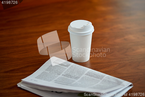 Image of coffee drink in paper cup and newspaper on table