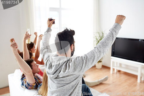 Image of happy friends with beer watching tv at home