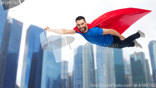 Image of happy man in red superhero cape flying over city