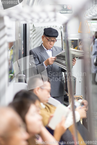 Image of Japanese businessman taking ride to work in morning, standing inside public transport and reading newspaper.