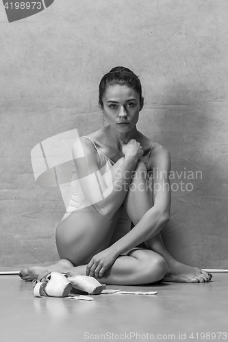 Image of Tired ballet dancer sitting on the wooden floor on a pink background