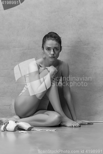 Image of Tired ballet dancer sitting on the wooden floor on a pink background