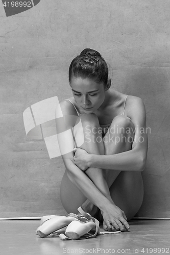 Image of Tired ballet dancer sitting on the wooden floor on a pink background