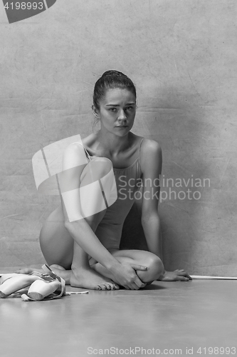 Image of Tired ballet dancer sitting on the wooden floor on a pink background