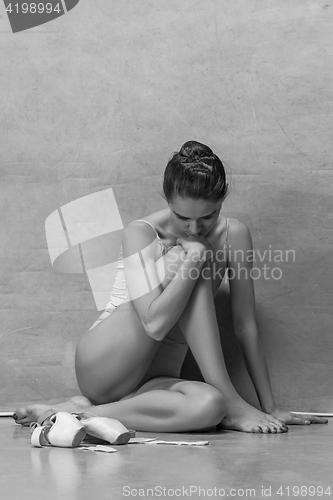 Image of Tired ballet dancer sitting on the wooden floor on a pink background