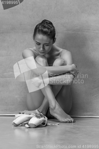 Image of Tired ballet dancer sitting on the floor on a pink background