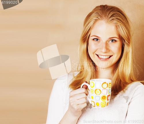 Image of young cute blond girl drinking coffee close up on warm brown bac