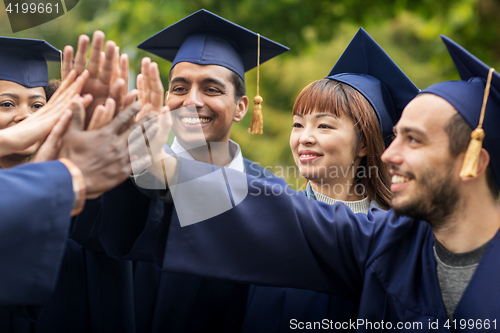 Image of happy students in mortar boards making high five