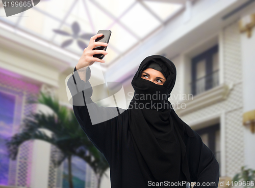 Image of muslim woman in hijab taking selfie by smartphone