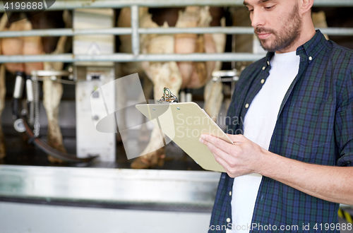 Image of young man with clipboard and cows on dairy farm