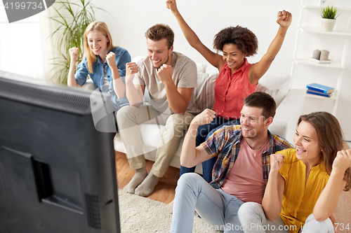 Image of happy friends with remote watching tv at home