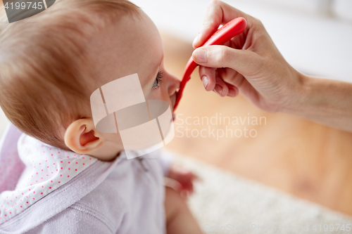 Image of hand with spoon feeding little baby at home