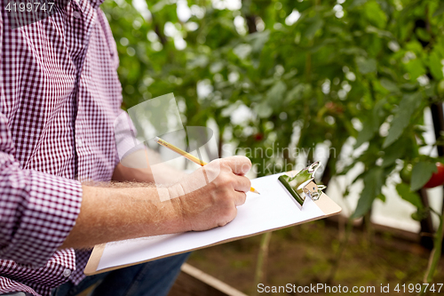 Image of senior man writing to clipboard at farm greenhouse