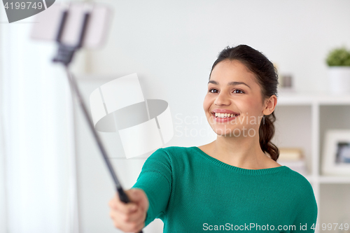 Image of woman taking selfie by smartphone monopod at home