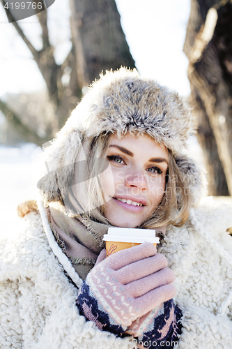 Image of young pretty teenage hipster girl outdoor in winter snow park having fun drinking coffee, warming up happy smiling, lifestyle people concept