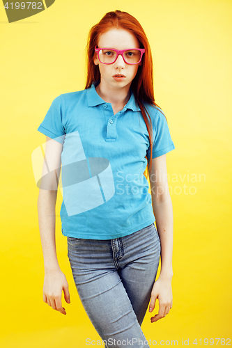 Image of young pretty red hair teenage hipster girl posing in glasses emotional happy smiling on yellow background, lifestyle people concept 