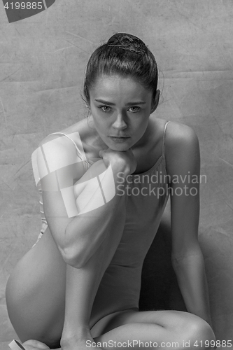 Image of Tired ballet dancer sitting on the wooden floor on a pink background