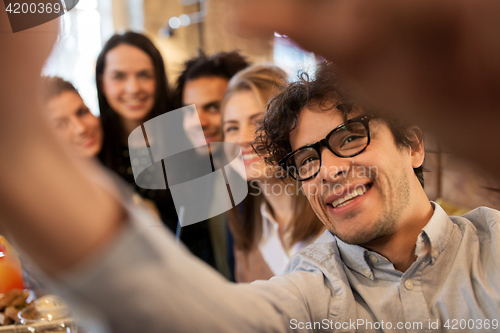 Image of happy man taking selfie with friends at restaurant