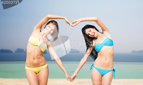 Image of happy women making heart shape on summer beach