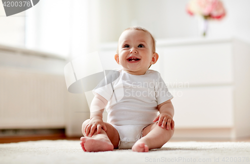 Image of happy baby boy or girl sitting on floor at home
