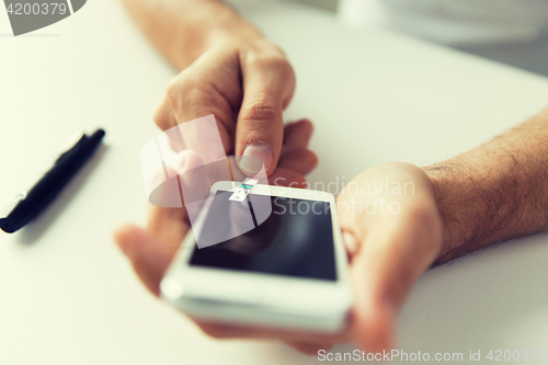 Image of close up of man with smartphone making blood test