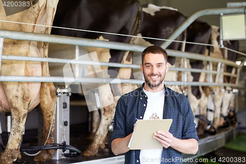 Image of man with clipboard and milking cows on dairy farm