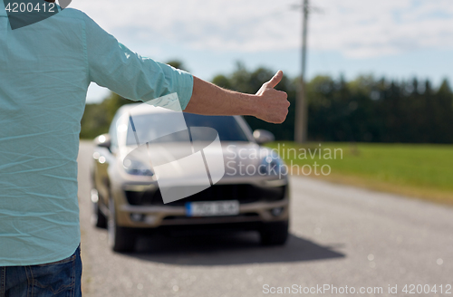 Image of man hitchhiking and stopping car with thumbs up