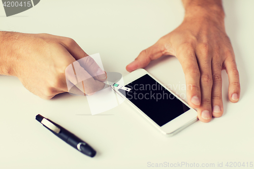 Image of close up of man with smartphone making blood test