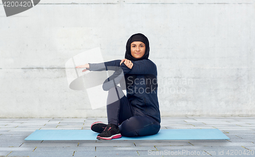 Image of muslim woman doing sportand stretching on mat