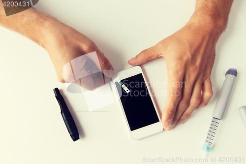 Image of close up of man with smartphone making blood test
