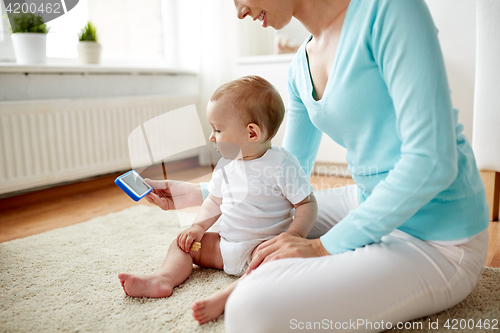 Image of happy mother showing smartphone to baby at home