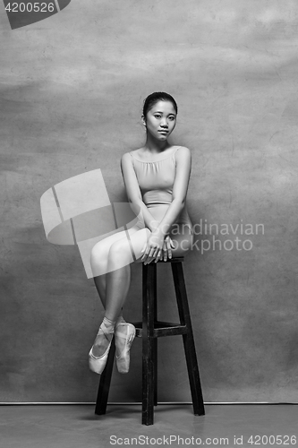 Image of Tired ballet dancer sitting on the wooden chair on a pink background