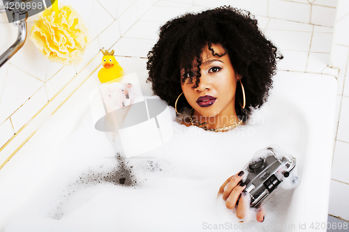 Image of young afro-american teen girl laying in bath with foam, wearing 