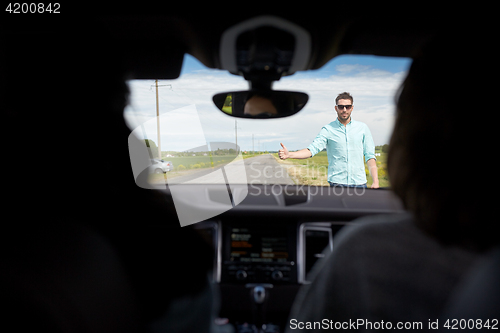 Image of man hitchhiking and stopping car with thumbs up