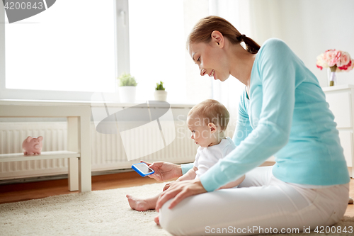 Image of happy mother showing smartphone to baby at home