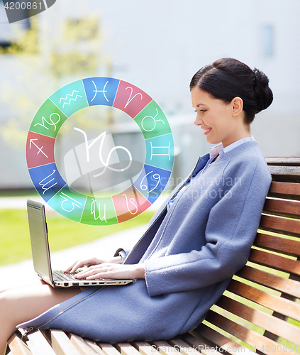 Image of smiling woman with laptop and zodiac signs in city