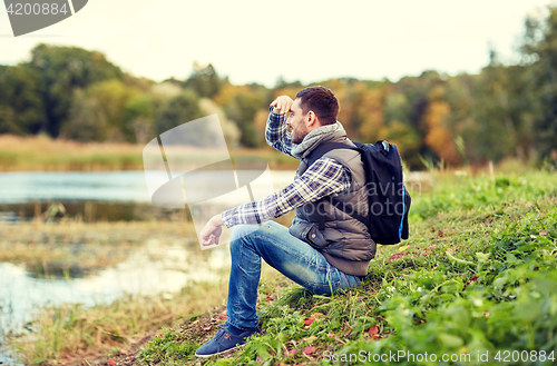 Image of smiling man with backpack resting on river bank