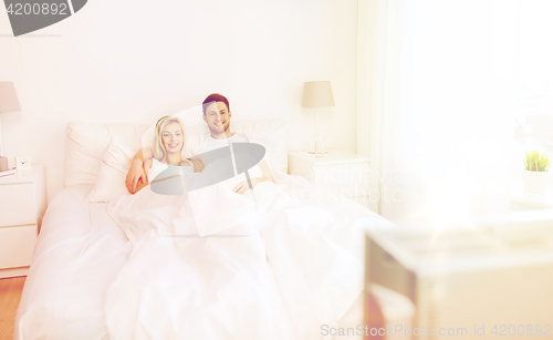 Image of happy couple lying in bed at home and watching tv