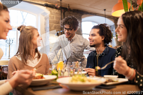 Image of happy friends eating and drinking at restaurant