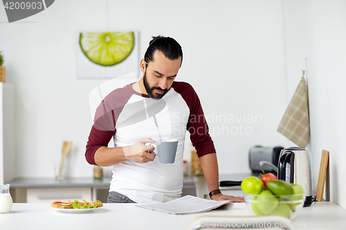 Image of man reading newspaper and eating at home kitchen