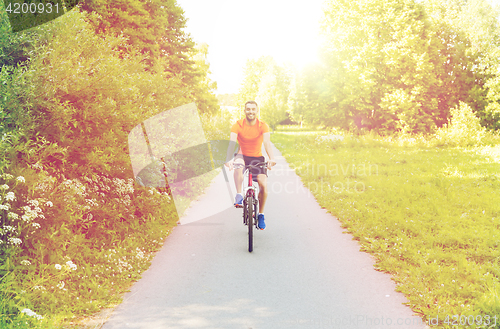 Image of happy young man riding bicycle outdoors