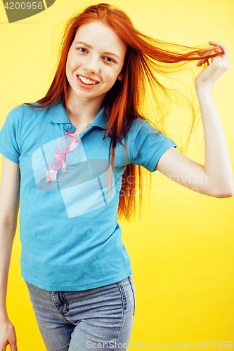Image of young pretty red hair teenage hipster girl posing in glasses emotional happy smiling on yellow background, lifestyle people concept 